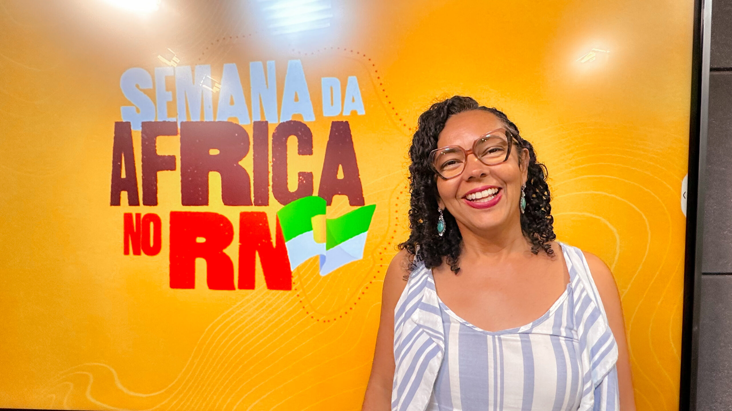 Mostra a deputada Divaneide Basílio a frente de banner da Semana da África no RN